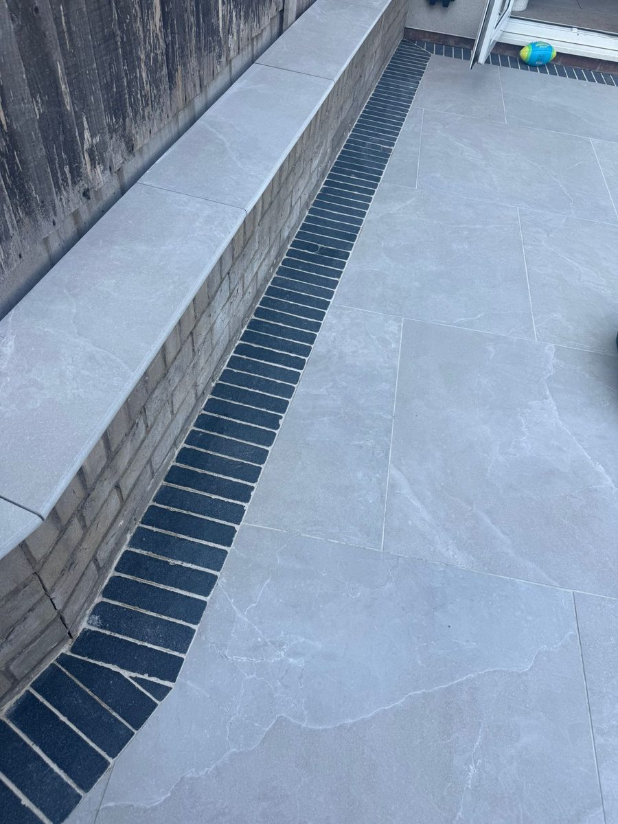 Grey porcelain patio with charcoal-slate border and channel drainage installed by Prostone — view 1