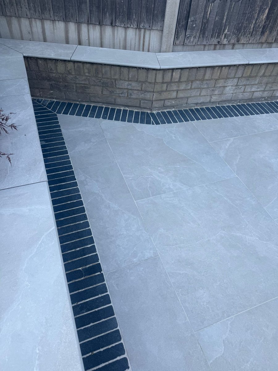Grey porcelain patio with charcoal-slate border and channel drainage installed by Prostone — view 3