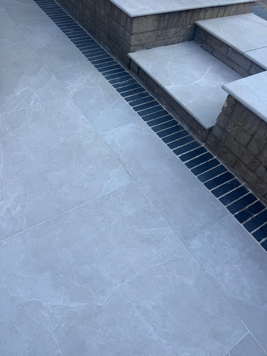 Grey porcelain patio with charcoal-slate border and channel drainage installed by Prostone — view 4