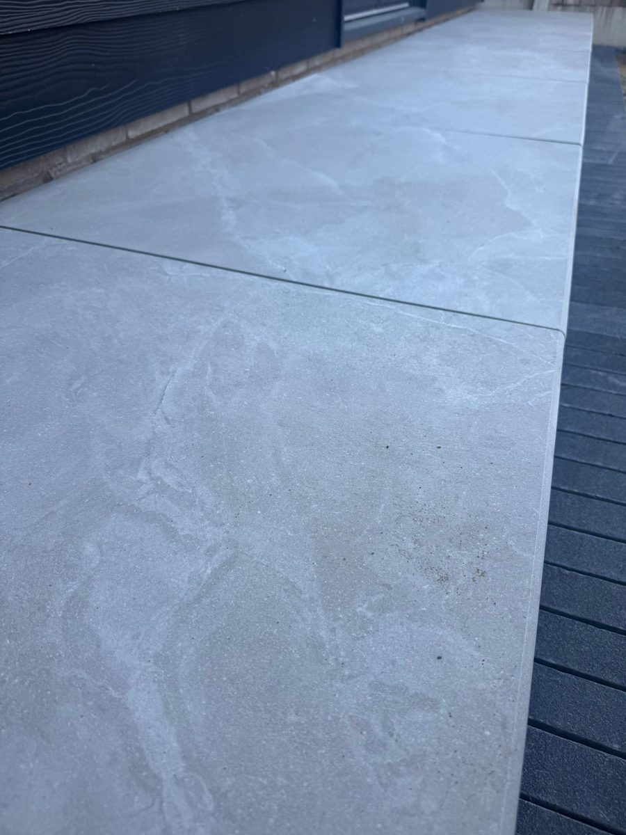 Grey porcelain patio with charcoal-slate border and channel drainage installed by Prostone — view 7
