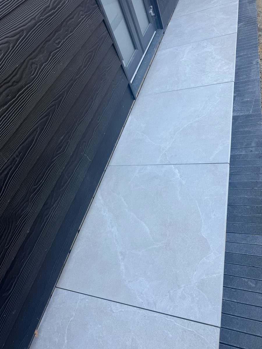 Grey porcelain patio with charcoal-slate border and channel drainage installed by Prostone — view 8